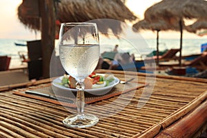 Beach evening on the sunset with glass of water and dinner