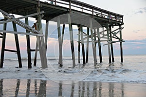 The beach fishing pier looms over the waves and sandy shoreline