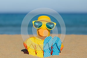 Beach flip-flops and yellow duck on the sand against blue sea and sky