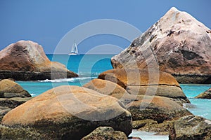 Beach in front of the Seychelles white sail boat sails off the coast on the blue sea