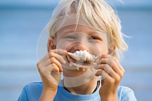 Beach fun, cute child holding shell over his mouth