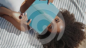 Beach girl reading book lying on blanket closeup. Playful smiling woman relax