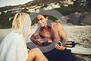 The beach, a guitar and you are all I need. a happy young couple serenading each other during a date on the beach at