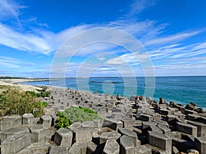 A beach half-filled with tetrapod and sandy at the other side facing the Pacific Ocean with a lighthouse in sight under