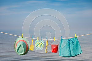 Beach hat, flip-flops and goggles hanging on a clothesline against sea and sky