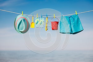 Beach hat, flip-flops and goggles hanging on a clothesline against sea and sky