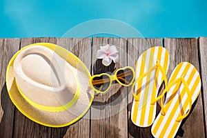 Beach hat, flip-flops and sunglasses on wooden planks near swimming pool