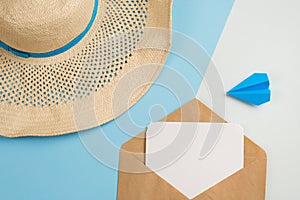 Beach hat, postcard in the envelope and the plane on a blue background. concept of flight on vacation and travel