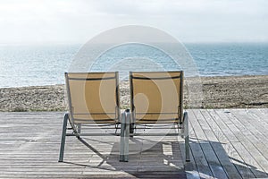 Beach holiday concept: two lounge chairs on the terrace in front of the blue sea