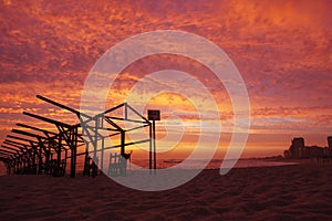 Beach hut frames silhouetted against vivid red sunset sky with dramatic clouds