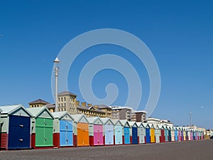 Beach huts lined up below clear blue sky.