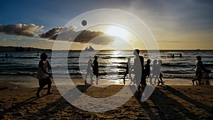 Beach on the island of Boracay in the rays of the evening sunset. Silhouettes of people playing a ball on the beach and