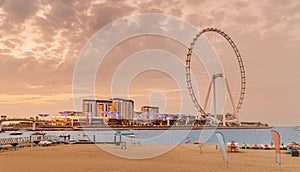 beach in JBR district and famous Dubai Eye Ferris Wheel during cloudy weather at sunset