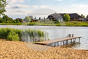 Beach and lake with pier, reeds, forest and wooden house