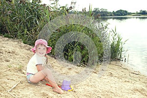 The beach at the lake in the sand a little girl in a hat playin