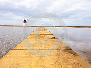 Beach landscape and wooden footbridge to reach the coast with lifeguard post and green flag allowing swimming. Canary Islands,
