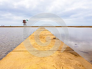 Beach landscape and wooden footbridge to reach the coast with lifeguard post and green flag allowing swimming. Canary Islands,