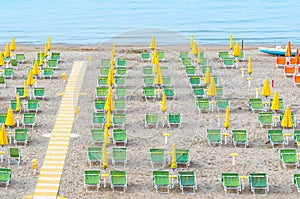 Beach lounge area with yellow umbrellas and green sunbeds on italian coastline.