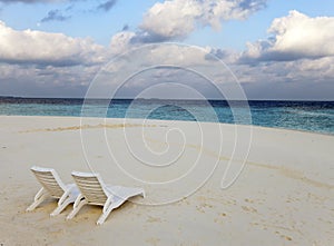 Beach lounge chairs on a beautiful tropical sand beach with cloudy blue sky. Maldives