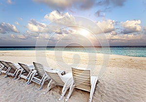 Beach lounge chairs on a beautiful tropical sand beach with cloudy blue sky. Maldives