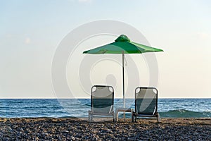 Beach lounge chairs under green umbrellas on the seashore, blue clear sky copy space
