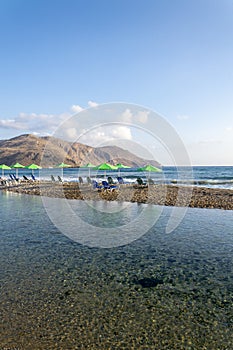 Beach lounge chairs under umbrellas on sandy peninsula between sea and river near Georgioupoli, Crete