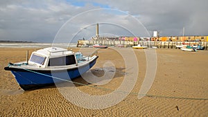 The beach at low tide with mooring boats and Margate Harbor Arm in the background, Margate, Kent, UK
