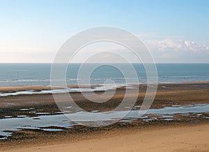 Beach at low tide with pools of water next to a calm blue sea and blue sky