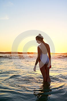 The beach makes me revisit all the good memories. a young woman standing in the water at sunset.