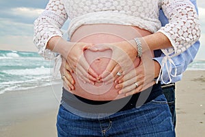 Beach Maternity Session. Pregnant Mom with Heart Symbol over Belly