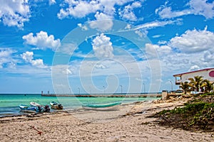 Beach in Mexico with Pier and building in distance and fishing boats tied up to shore under beautiful sky with pile of seaweed on
