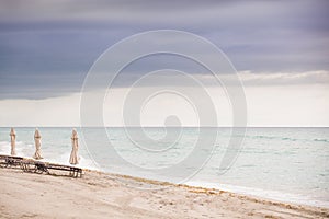 Beach in Miami, FL. Folded umbrellas on the sand beach at the ocean. Empty beach. Sea shore. Early morning. Clouds