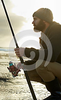 Beach, ocean and man with fishing rod in water in the morning in summer outdoor for hobby or leisure. Sea, fisherman and