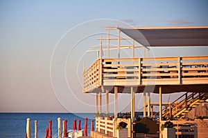 Beach before the opening, folded sun loungers and umbrellas, empty tables in a cafe