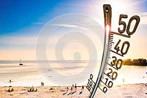 Beach with people, bright sun and a big thermometer