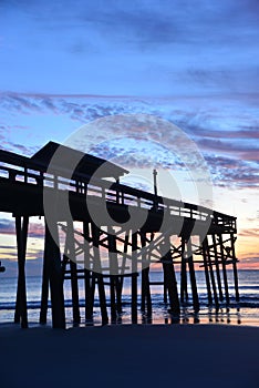 The beach pier appears like a skyscraper when framed by the sunrise over the ocean