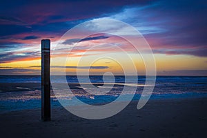 Beach pole during sunset with foam heads on the sand beach on the Dutch Island of Texel beach