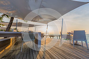 Beach restaurant, sunset light and soft colors on wooden deck with white furniture and sea view