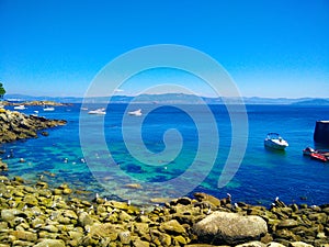 Beach of rocks in Cies Islands, Galicia, Spain, with boats diving in front of it