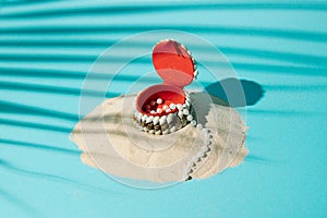 Beach sand with a box of shells and with pearls coming out of the box on a blue background with palm leaf shadow. Summer minimal