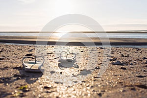 on beach on the sand a pair of beach slippers stands close-up and the background is blurred at sunset, the photo is