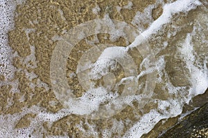 Beach sand sea water summer background. Sand beach desert texture. White foam wave sandy seashore top view.