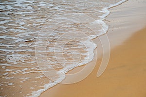 Beach sand sea water summer background. Sand beach desert texture. White foam wave sandy seashore top view. A sunny