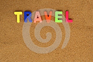 On the beach sand is written a word of bright letters the word travel.