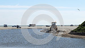 Beach scene with a front end loader and vehicles on the sand by ocean.