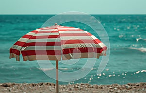 a beach scene with a red and white striped umbrella