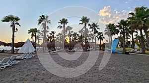 Beach scene with sunset sky, palm trees and lounge chairs