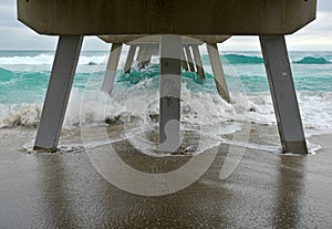 Beach scene with wooden fishing pier and waves in Atlantic Ocean in Florida