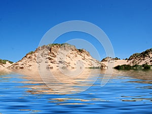 Beach from the sea at formby merseyside with tall sand dunes covered in rough grass and a blue summer sunlit sky