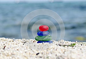 Beach seaglass zen cairn. Sea glass pyramid on sea shore on blurred sea background. Zen sculpture, a seaglass tower